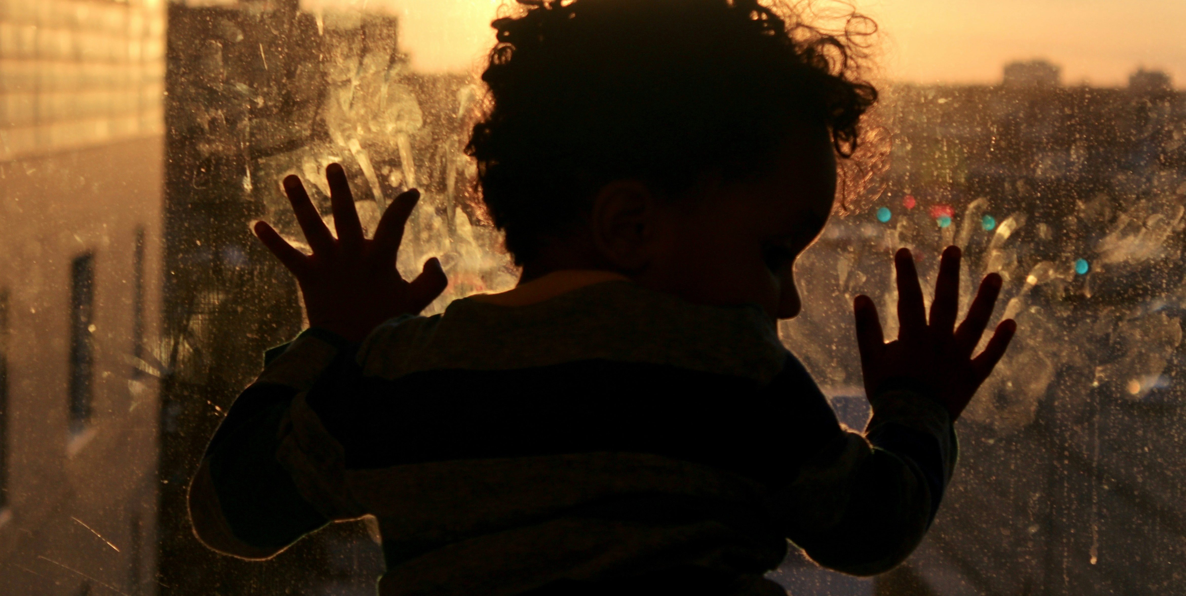 Silueta de un niño mirando por una ventana al atardecer